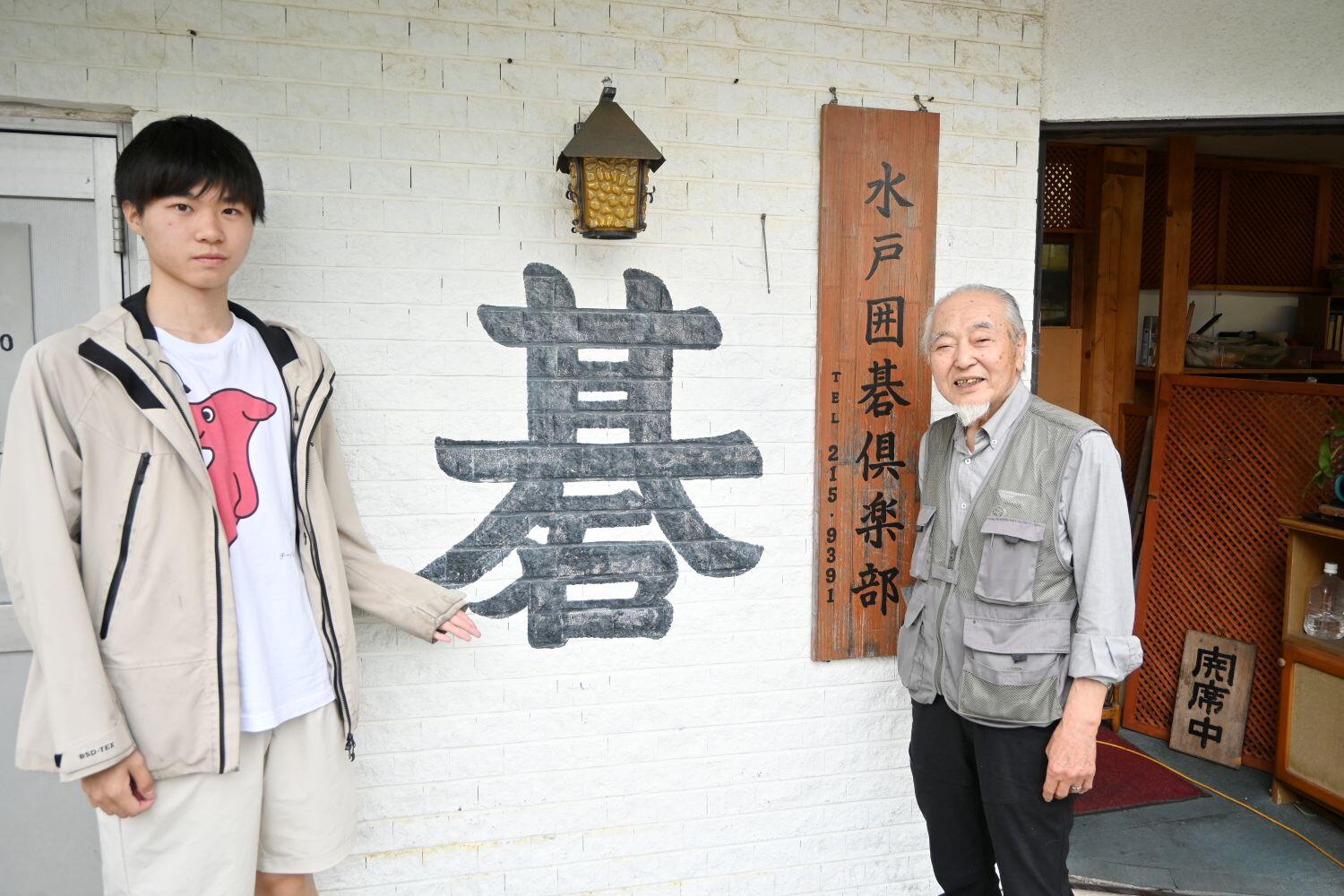 水戸囲碁倶楽部のシンボル大きな「碁」の字を挟んで写真を撮る２人
